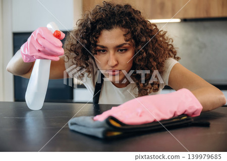 Cleaning the surface. White woman on the the kitchen countertop with spray and cloth wearing pink gloves Cleaning the surface. White woman on the the kitchen countertop with spray and cloth wearing pink gloves 139979685