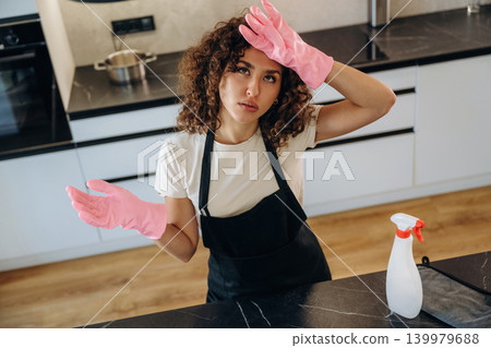 Very tired. White woman cleaning the kitchen countertop with spray and cloth wearing pink gloves Very tired. White woman cleaning the kitchen countertop with spray and cloth wearing pink gloves 139979688
