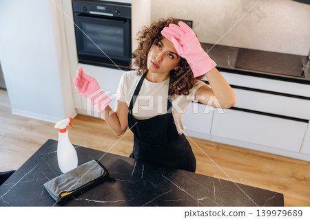Very tired. White woman cleaning the kitchen countertop with spray and cloth wearing pink gloves 139979689