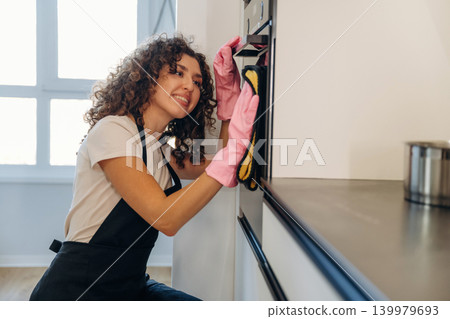 Routine time. White woman cleaning the kitchen countertop with spray and cloth wearing pink gloves Routine time. White woman cleaning the kitchen countertop with spray and cloth wearing pink gloves 139979693