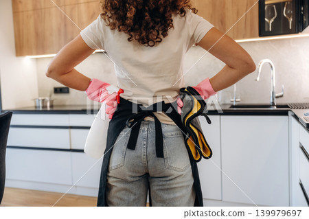 Woman wearing cleaning gloves and apron standing in a modern kitchen, preparing for household chores 139979697