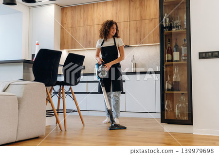 Housewife is vacuuming the floor and cleaning around furniture in a modern kitchen and dining area 139979698