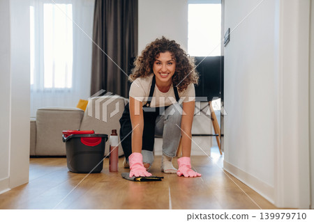 Busy woman cleaning the floor on her knees with a bucket and cloth during household chores 139979710