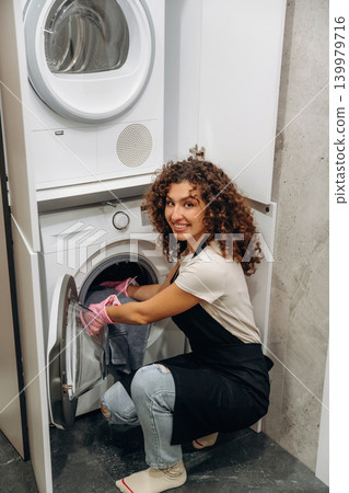 Smiling, cheerful facial expression. At home. Woman doing laundry with washing machine at home Smiling, cheerful facial expression. At home. Woman doing laundry with washing machine at home 139979716