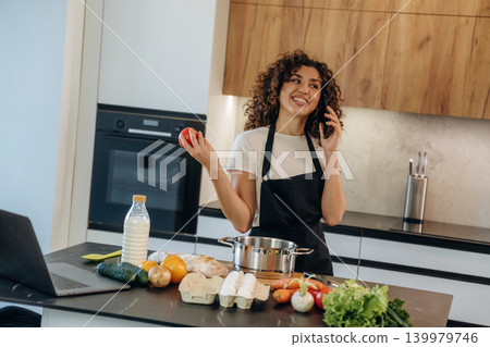 Talking by phone. Attractive woman preparing fresh vegetables on the kitchen counter during cooking 139979746