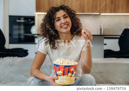 Tasty meal. Happy woman relaxing on a sofa with popcorn, watching TV and enjoying her leisure time at home 139979759