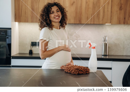 Curly hair. Pregnant woman wiping the kitchen counter while doing household chores at home 139979806