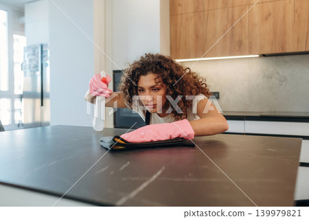 Cleaning the surface. White woman on the the kitchen countertop with spray and cloth wearing pink gloves Cleaning the surface. White woman on the the kitchen countertop with spray and cloth wearing pink gloves 139979821