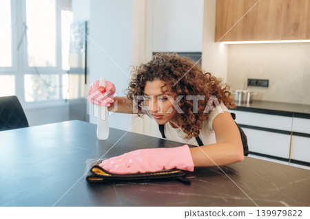 Cleaning the surface. White woman on the the kitchen countertop with spray and cloth wearing pink gloves 139979822