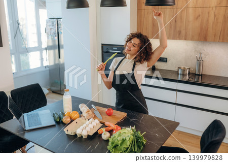 Having fun, singing. Attractive woman preparing fresh vegetables on the kitchen counter during cooking Having fun, singing. Attractive woman preparing fresh vegetables on the kitchen counter during cooking 139979828