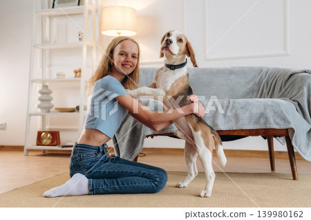 Smiling, having fun. Girl is with her dog on the floor in a cozy living room Smiling, having fun. Girl is with her dog on the floor in a cozy living room 139980162