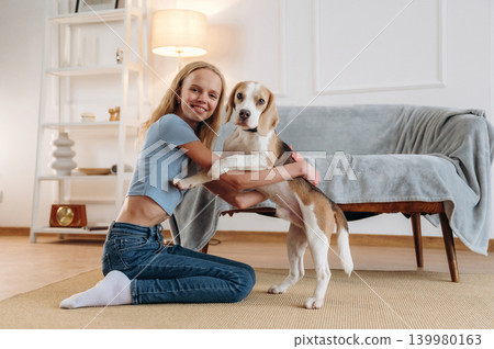 Smiling, having fun. Girl is with her dog on the floor in a cozy living room Smiling, having fun. Girl is with her dog on the floor in a cozy living room 139980163