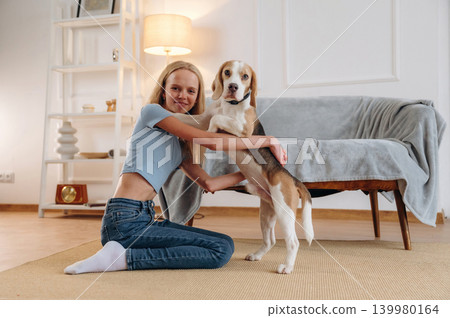 Smiling, having fun. Girl is with her dog on the floor in a cozy living room 139980164
