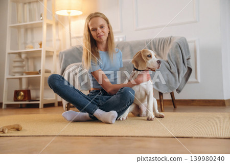 Casual time spending, wellness. Girl is with her dog on the floor in a cozy living room Casual time spending, wellness. Girl is with her dog on the floor in a cozy living room 139980240