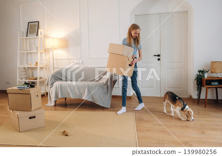 Walking and holding the box. Young girl is moving into new home with her dog Walking and holding the box. Young girl is moving into new home with her dog 139980256