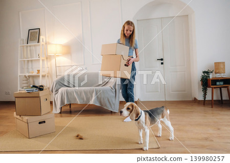 Walking and holding the box. Young girl is moving into new home with her dog Walking and holding the box. Young girl is moving into new home with her dog 139980257