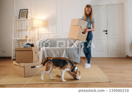 Walking and holding the box. Young girl is moving into new home with her dog Walking and holding the box. Young girl is moving into new home with her dog 139980258