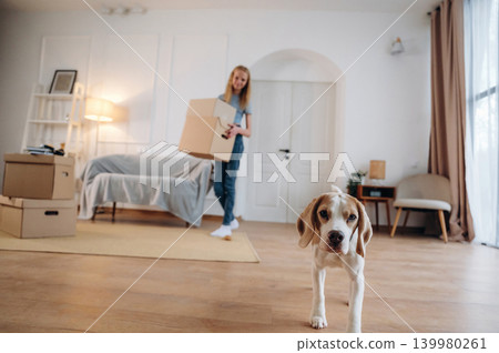 Walking and holding the box. Young girl is moving into new home with her dog Walking and holding the box. Young girl is moving into new home with her dog 139980261