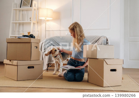 Bunch of boxes, new home, relocation. Girl is with her dog on the floor in a cozy living room Bunch of boxes, new home, relocation. Girl is with her dog on the floor in a cozy living room 139980266