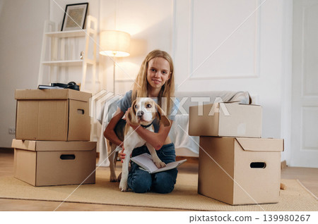 Bunch of boxes, new home, relocation. Girl is with her dog on the floor in a cozy living room Bunch of boxes, new home, relocation. Girl is with her dog on the floor in a cozy living room 139980267