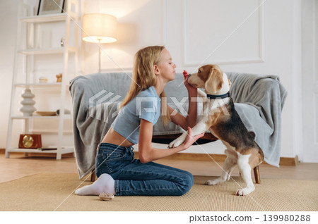 Teaching the tricks. Girl is with her dog on the floor in a cozy living room Teaching the tricks. Girl is with her dog on the floor in a cozy living room 139980288