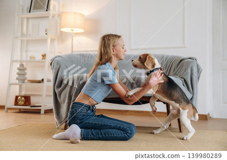 Teaching the tricks. Girl is with her dog on the floor in a cozy living room Teaching the tricks. Girl is with her dog on the floor in a cozy living room 139980289
