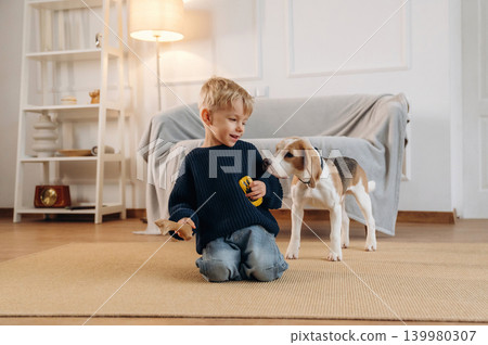 Yellow toy car holding in hand. Cute little boy playing with dog at home on the floor 139980307