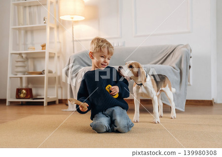 Yellow toy car holding in hand. Cute little boy playing with dog at home on the floor 139980308