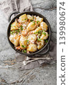 Homemade new potatoes with creamy mushroom sauce, bacon, and breadcrumbs, close-up, in a frying pan. Vertical top view 139980674