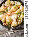 Baked potatoes in a creamy mushroom sauce with bacon sprinkled with breadcrumbs and parsley close-up in a frying pan on the table. Vertical top view 139980676