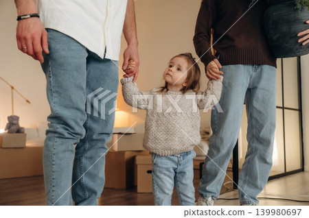 Particle view, holding kid by hands. Happy young family with child and dog moving into new home, standing among cardboard boxes Particle view, holding kid by hands. Happy young family with child and dog moving into new home, standing among cardboard boxes 139980697