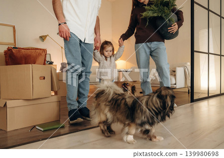 Particle view, holding kid by hands. Happy young family with child and dog moving into new home, standing among cardboard boxes Particle view, holding kid by hands. Happy young family with child and dog moving into new home, standing among cardboard boxes 139980698