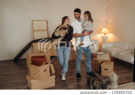 Cute dog is in hands. Happy young family with child moving into new home, standing among cardboard boxes Cute dog is in hands. Happy young family with child moving into new home, standing among cardboard boxes 139980708