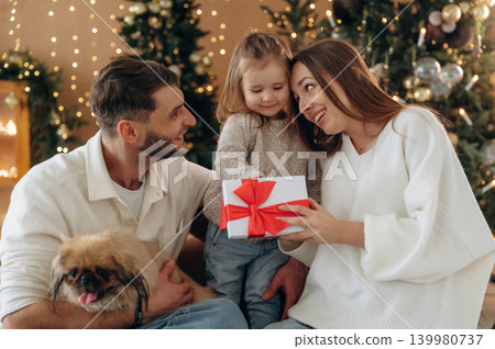 Surprise, the present in gift box. Happy family with child and dog celebrating Christmas together at home with decorated tree Surprise, the present in gift box. Happy family with child and dog celebrating Christmas together at home with decorated tree 139980737