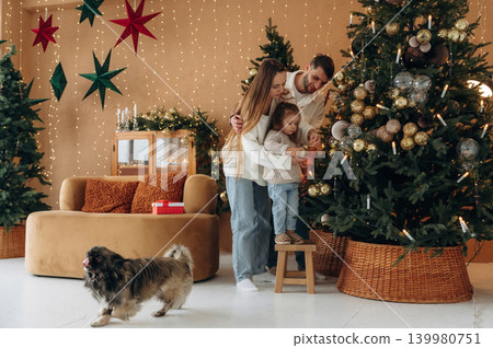 Happy family with child and dog celebrating Christmas together at home with decorated tree Happy family with child and dog celebrating Christmas together at home with decorated tree 139980751