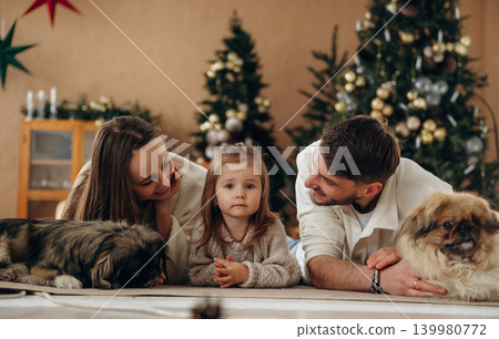 Front view, lying down. Happy family with child and dog celebrating Christmas together at home with decorated tree Front view, lying down. Happy family with child and dog celebrating Christmas together at home with decorated tree 139980772