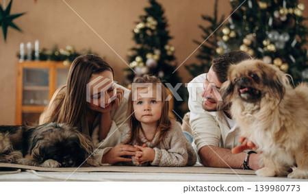 Front view, lying down. Happy family with child and dog celebrating Christmas together at home with decorated tree Front view, lying down. Happy family with child and dog celebrating Christmas together at home with decorated tree 139980773