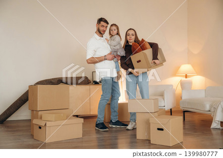 Cheerful young family with child moving into new home, standing among cardboard boxes Cheerful young family with child moving into new home, standing among cardboard boxes 139980777
