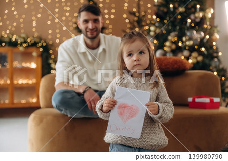 Little girl holding hand drawn picture, father's day, while at home with dad during Christmas holidays Little girl holding hand drawn picture, father's day, while at home with dad during Christmas holidays 139980790