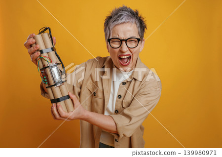 Excited woman with short gray hair holding a mock up of a dynamite stick, showcasing a playful and adventurous spirit against a vibrant yellow background Excited woman with short gray hair holding a mock up of a dynamite stick, showcasing a playful and adventurous spirit against a vibrant yellow background 139980971