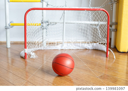 Children enjoy playing with a red basketball in a room that has a small goal. Children enjoy playing with a red basketball in a room that has a small goal. 139981097