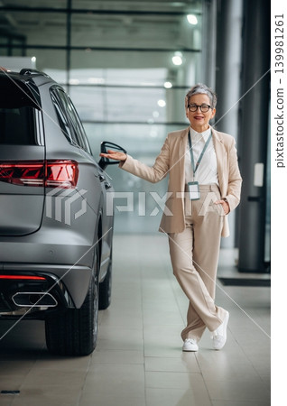 Confident woman in stylish suit stands beside luxury SUV in modern showroom, showcasing automotive elegance and professionalism in a sleek environment Confident woman in stylish suit stands beside luxury SUV in modern showroom, showcasing automotive elegance and professionalism in a sleek environment 139981261