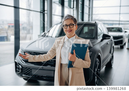 Confident female car sales representative presenting vehicle in modern showroom, showcasing professionalism and customer service in automotive industry Confident female car sales representative presenting vehicle in modern showroom, showcasing professionalism and customer service in automotive industry 139981268