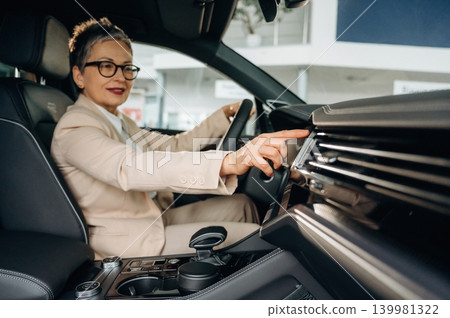 Businesswoman in stylish suit is confidently adjusting controls inside a modern car, showcasing the blend of luxury and technology in automotive design Businesswoman in stylish suit is confidently adjusting controls inside a modern car, showcasing the blend of luxury and technology in automotive design 139981322