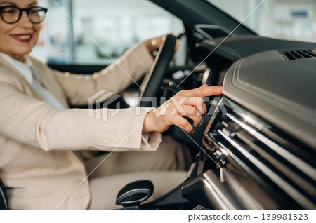 Businesswoman in stylish suit is adjusting car dashboard controls while seated in modern vehicle, showcasing interior features and technology Businesswoman in stylish suit is adjusting car dashboard controls while seated in modern vehicle, showcasing interior features and technology 139981323