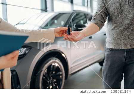 Handing over car keys in a modern dealership, showcasing a transaction between customer and salesperson, highlighting the excitement of new car ownership experience Handing over car keys in a modern dealership, showcasing a transaction between customer and salesperson, highlighting the excitement of new car ownership experience 139981354
