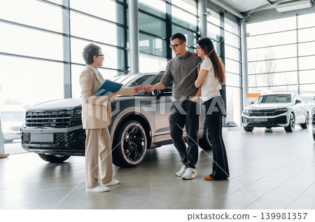 Couple discussing car purchase with sales representative in modern showroom, showcasing sleek vehicles and bright, spacious environment for an engaging shopping experience Couple discussing car purchase with sales representative in modern showroom, showcasing sleek vehicles and bright, spacious environment for an engaging shopping experience 139981357