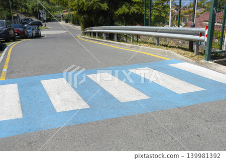 A brightly painted blue and white crosswalk is prominent in the foreground of the image. A brightly painted blue and white crosswalk is prominent in the foreground of the image. 139981392
