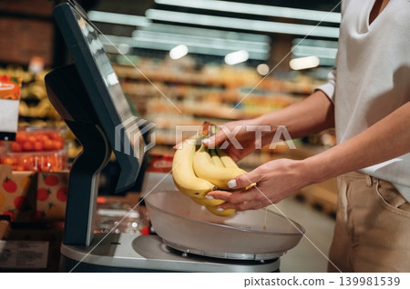 Individual weighing fresh bananas on digital scale in grocery store, surrounded by colorful produce, showcasing healthy shopping habits and modern technology Individual weighing fresh bananas on digital scale in grocery store, surrounded by colorful produce, showcasing healthy shopping habits and modern technology 139981539