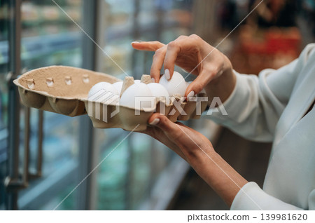 Woman selecting fresh eggs from carton in grocery store, showcasing careful choice and quality, emphasizing healthy food options and shopping experience Woman selecting fresh eggs from carton in grocery store, showcasing careful choice and quality, emphasizing healthy food options and shopping experience 139981620